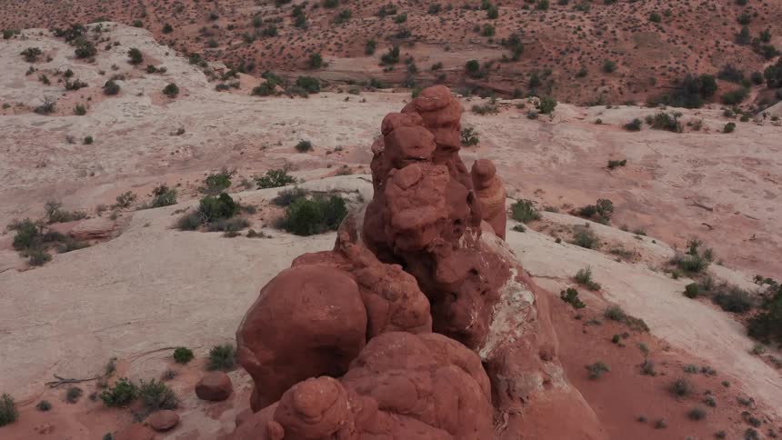A slow aerial orbit reveals the unique textures and shapes of a weathered red sandstone spire in a vast desert canyon
