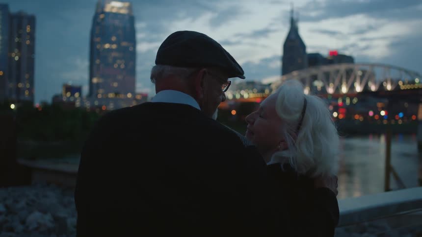 A man and woman hug and stand near the pier at dawn