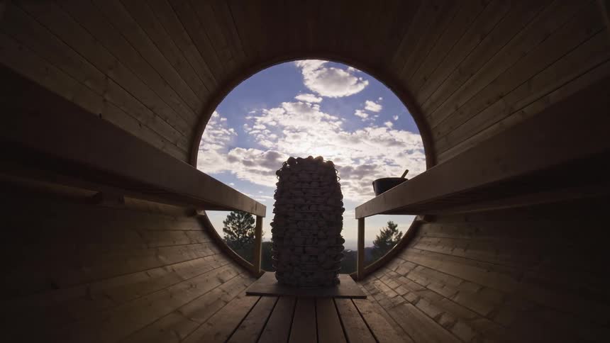 A slow dolly shot reveals the interior of a peaceful barrel sauna with a scenic view of the sky through its round window