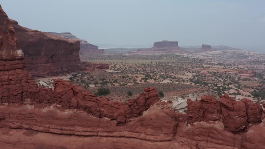 An aerial panning shot reveals the incredible red rock formations overlooking a vast desert valley in Moab, Utah