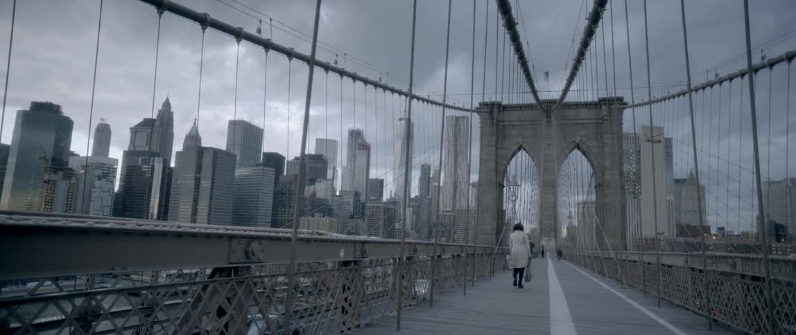 People walk down a bridge with skyscrapers in the background