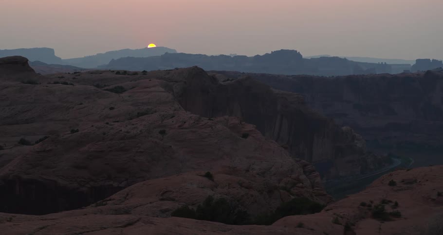 Aerial view slowly zooms out over a vast and hazy red rock canyon landscape at sunrise