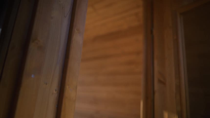 A person in a bathrobe slowly opens the wooden door and enters a warm, relaxing sauna