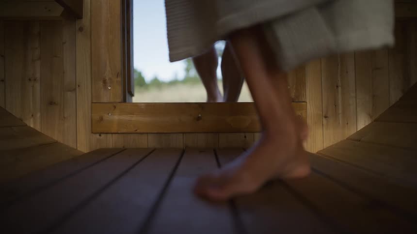 Slow motion, low-angle shot of a couple's bare feet meeting on the wooden floor as they enter a sauna together and close the door