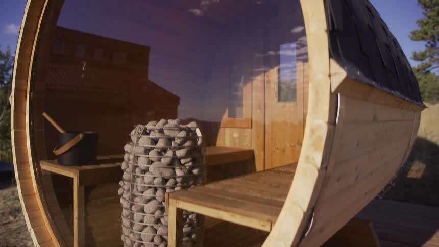 Slow cinematic reveal of a modern wooden barrel sauna with a panoramic glass window, sitting on an outdoor deck on a sunny day