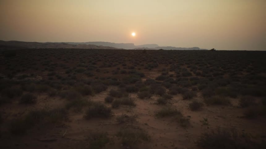 A serene timelapse captures the sun setting behind distant mountains in a vast, hazy desert landscape