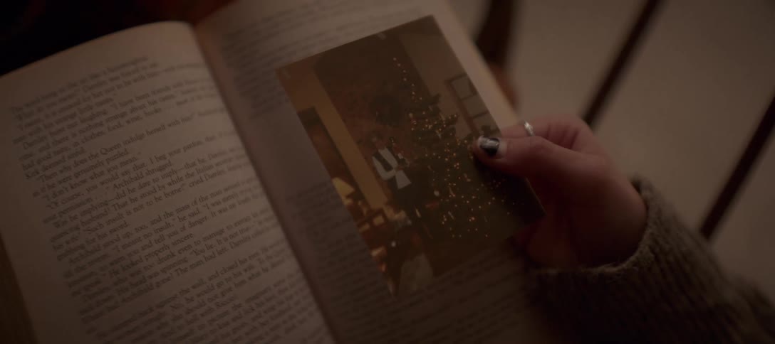 A person's hand holds a vintage Christmas photograph over the pages of an open book, evoking a sense of nostalgia
