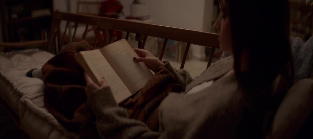 A woman relaxes on a cozy sofa, wrapped in a warm blanket, as she reads a book in her dimly lit living room at night