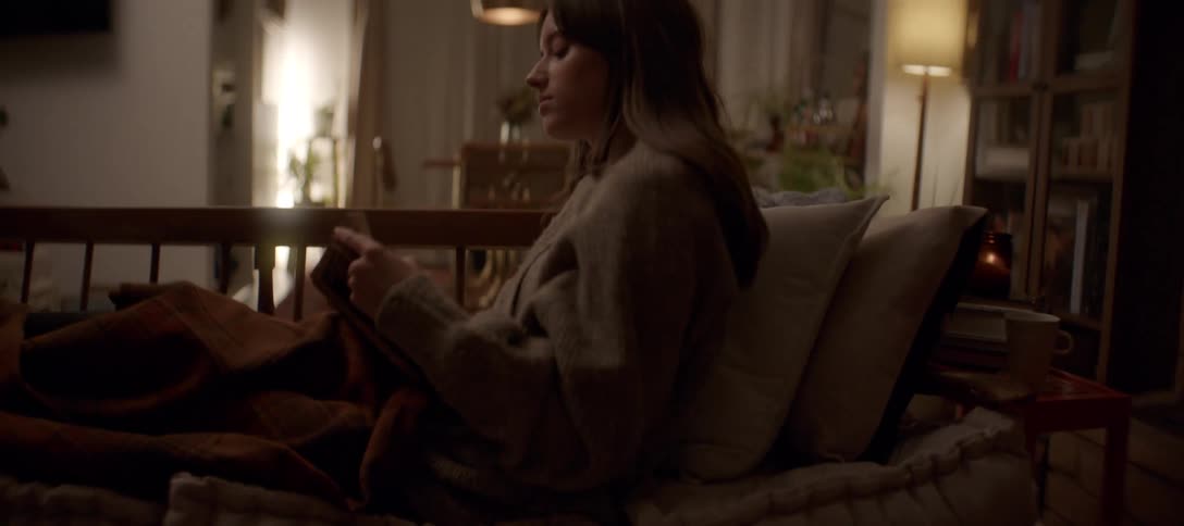 Cozy evening at home as a woman reads a book, lying comfortably on the sofa with a warm blanket