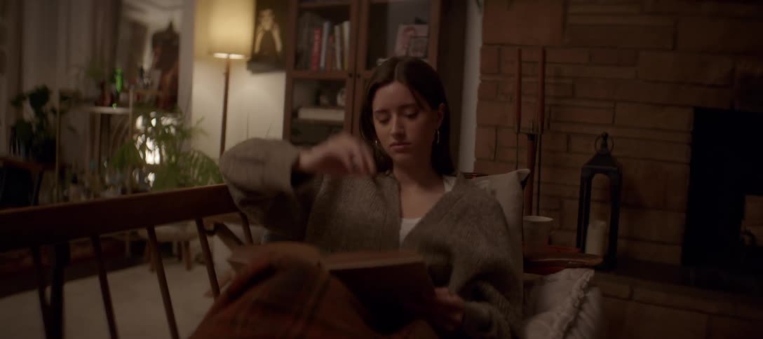 A young woman gets lost in a good book while relaxing under a blanket in a cozy chair at night
