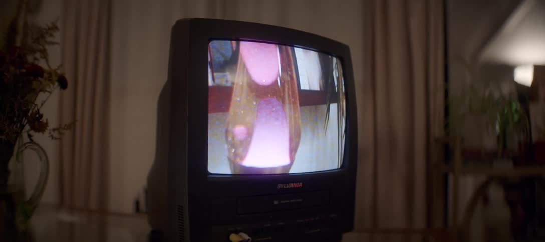 A mesmerizing video of a pink lava lamp plays on a vintage TV/VCR combo in a dimly lit, nostalgic room