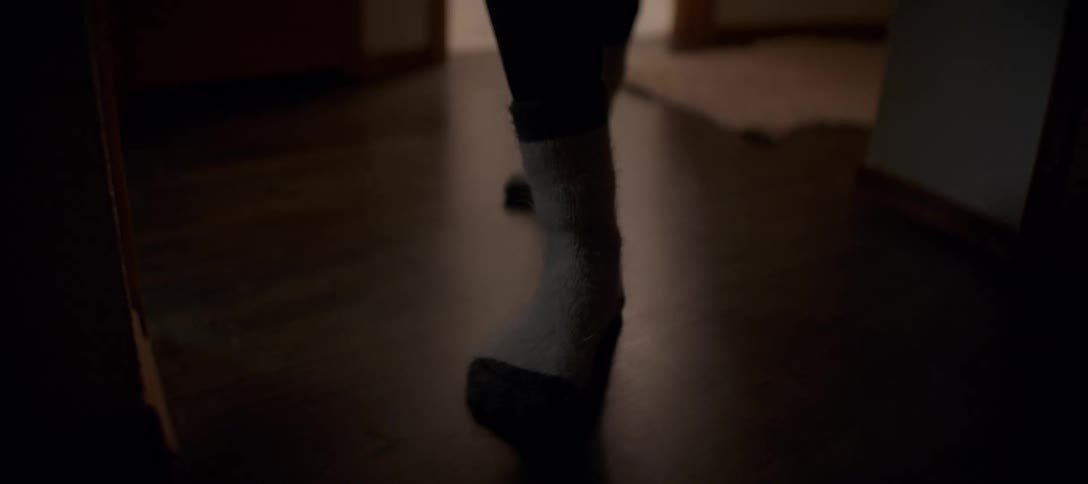 A close up slow motion shot of a person wearing socks walking through a dimly lit hallway