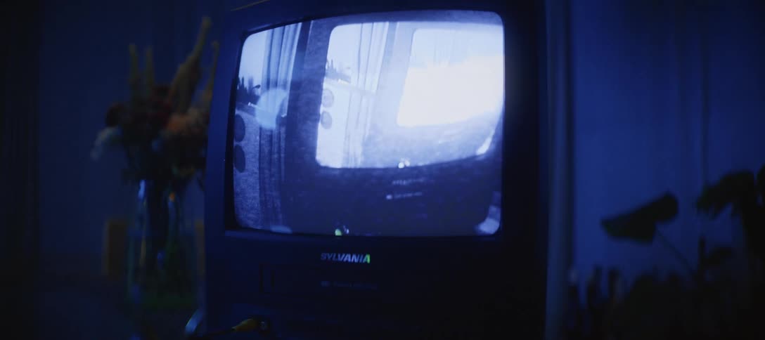 A vintage Sylvania TV/VCR combo displays a distorted home video in a dark room with a moody blue ambiance