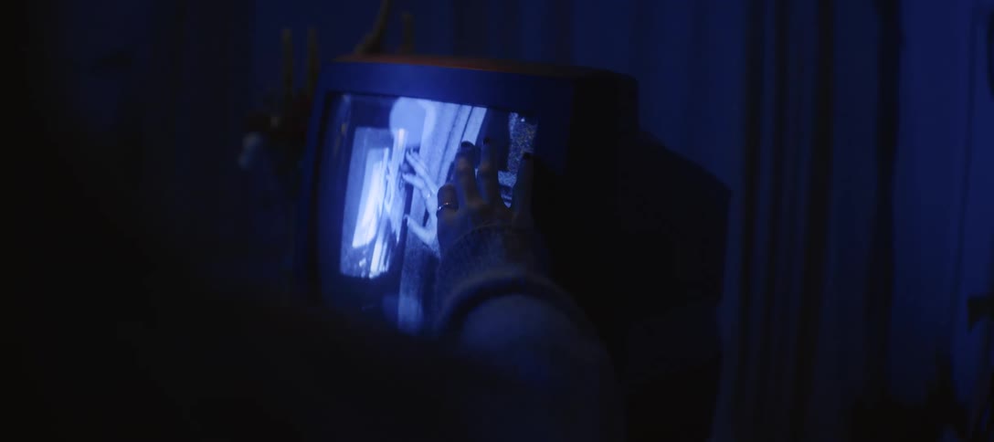 A person's hand touches the static-filled screen of a retro television glowing in a dark room