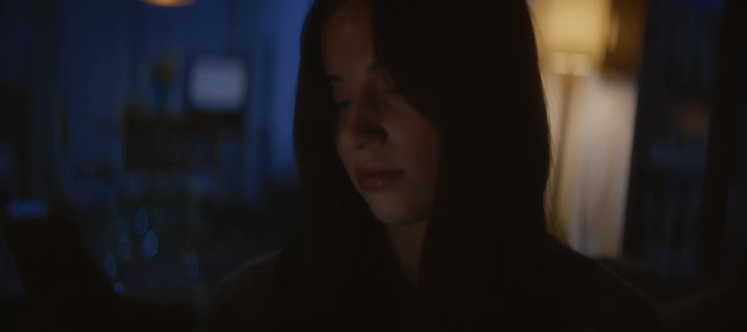 Close up of a young woman's face as she looks down at her phone, illuminated by the screen in a dark room