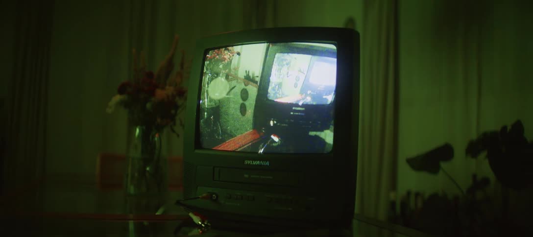 A retro CRT television with a built-in VCR displays a video feedback loop as the surrounding room is bathed in shifting colored lights