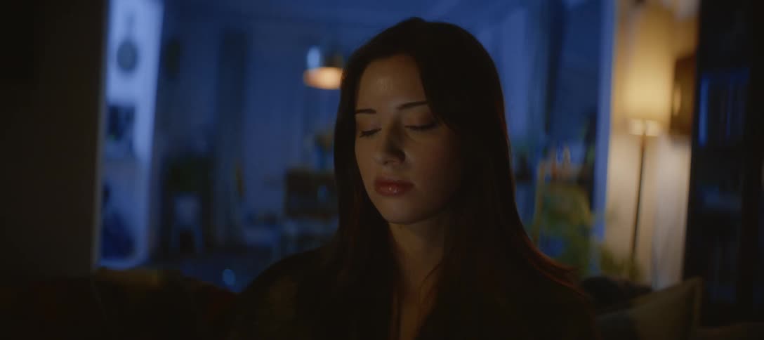 Close up of a sad young woman looking at her smartphone in a dimly lit living room at night