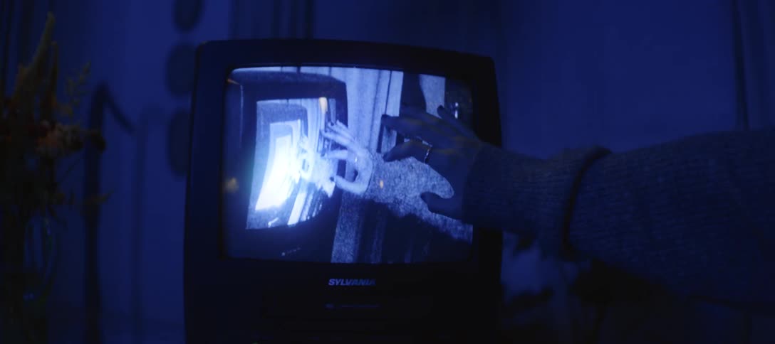 A surreal close-up of a hand touching a retro television displaying an endless video feedback loop in a dark room