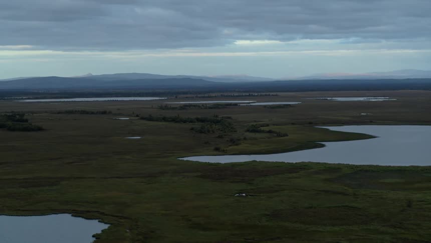 An aerial view of the majestic Alaskan landscape with its vast wetlands and countless lakes under a twilight sky