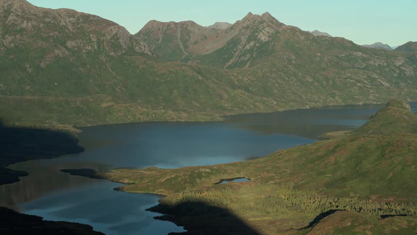Sunlight illuminates a beautiful valley with a large, calm lake nestled between green mountains