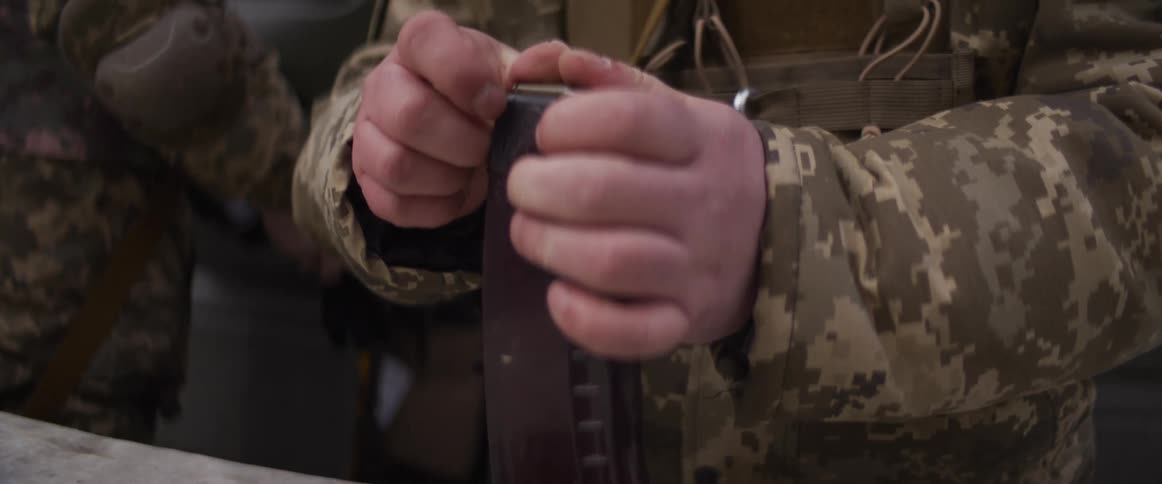 A slow-motion close-up captures a soldier's hands meticulously loading live ammunition into a rifle magazine