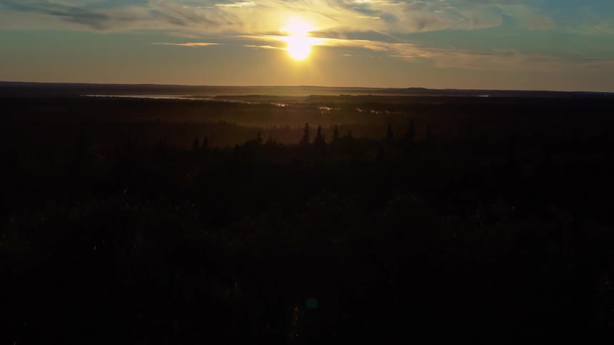 A slow aerial ascent reveals a beautiful sunset over a vast forest and distant lake
