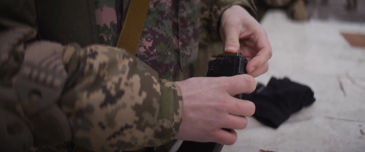 A soldier in a camouflage uniform carefully loads bullets into a rifle magazine in a slow-motion close-up