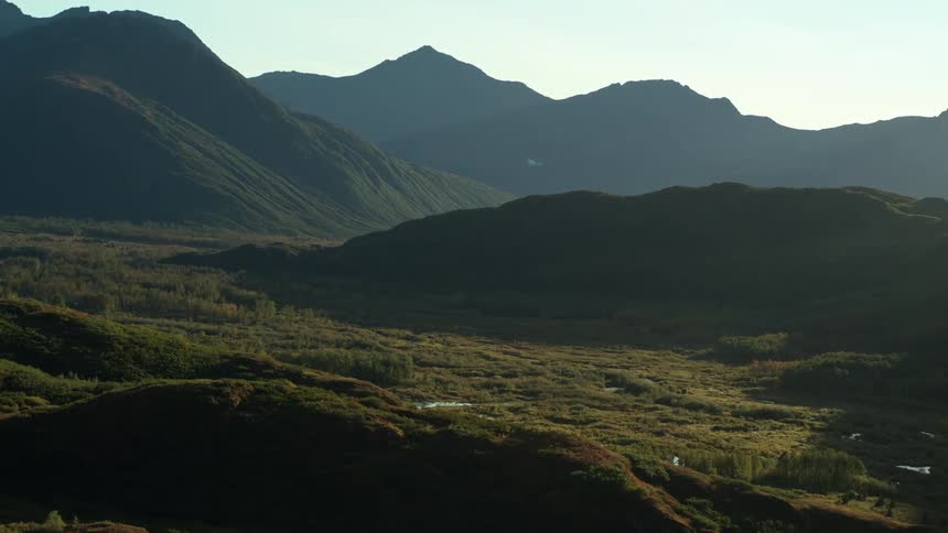 An epic aerial shot slowly reveals a vast, wild valley nestled between silhouetted mountains in the early morning light