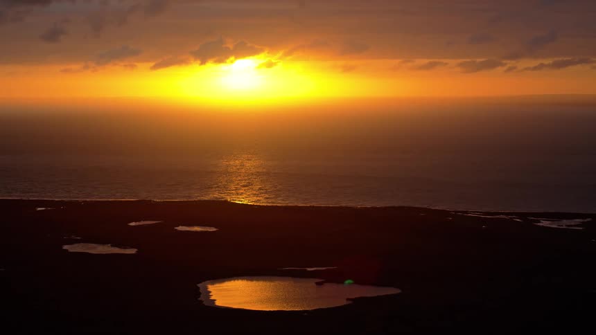 A beautiful golden sunset glows over the ocean, its light reflecting in small ponds along the silhouetted coastline