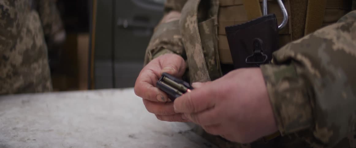 Close up of a soldier's hands in a camouflage uniform carefully loading bullets into a magazine