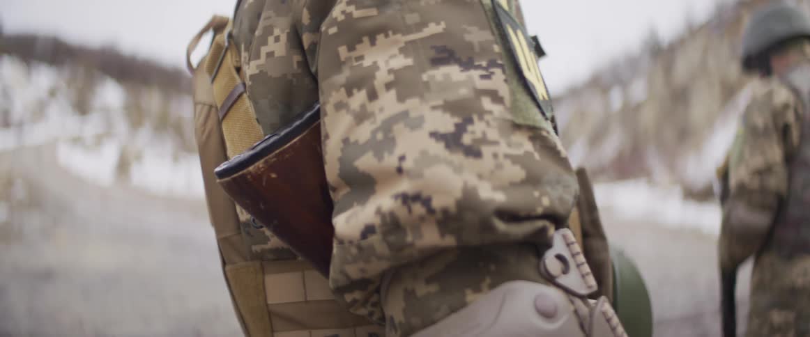 Slow motion close-up of a Ukrainian soldier in full combat gear, including a camouflage uniform, tactical vest, and rifle