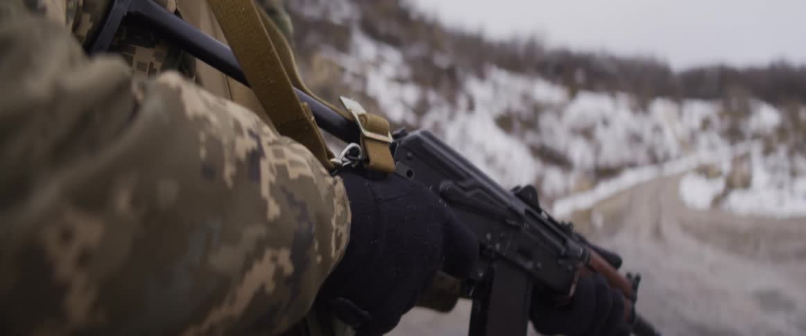 A soldier in camouflage wearing gloves reloads an assault rifle in a snowy, winter landscape
