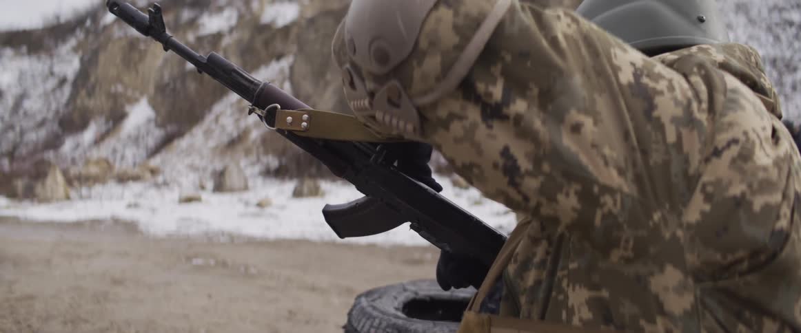 A Ukrainian soldier in full combat gear fires a rifle in slow motion during a military training exercise in a snowy environment