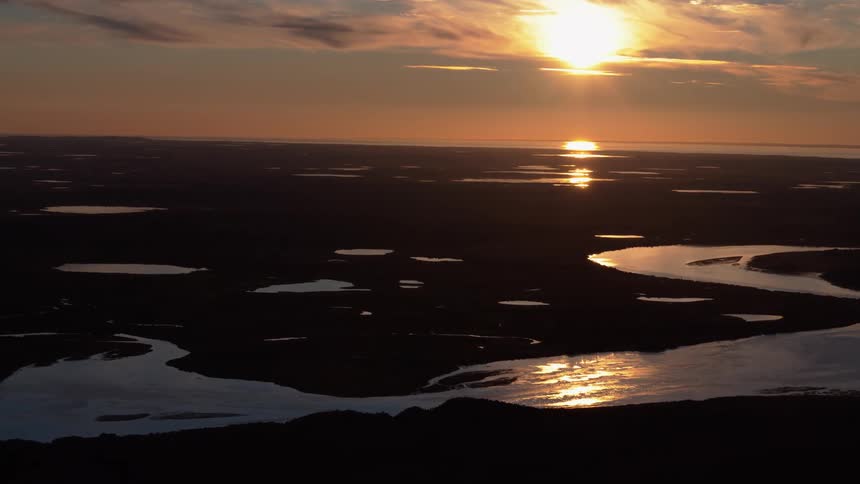 A serene sunset reflects off winding rivers and lakes in a vast, silhouetted delta landscape