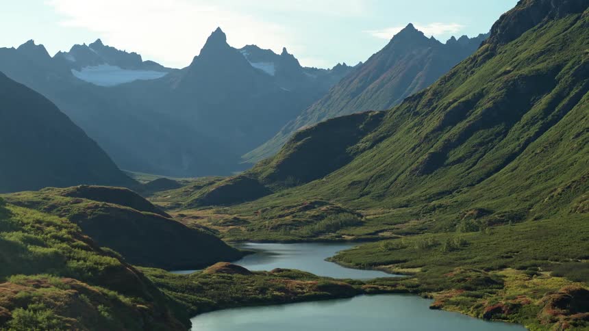 Sweeping aerial shot reveals a tranquil lake and verdant valley nestled within a majestic mountain range