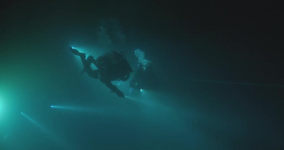 Bright beams from flashlights cut through the dark, murky water as scuba divers explore an underwater cave