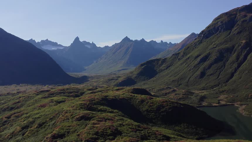 An epic aerial view pulls back to reveal a vast and pristine mountain valley with a serene lake and rugged peaks