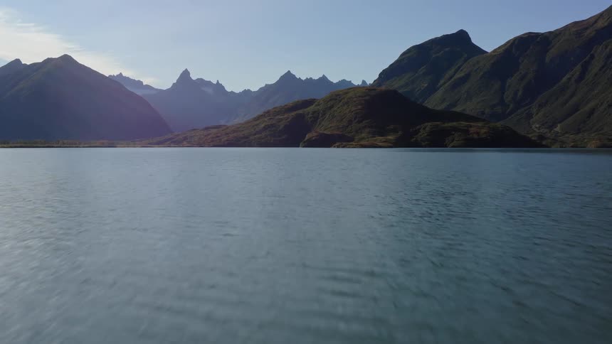 A serene aerial journey over a vast lake surrounded by majestic, rugged mountains on a clear day