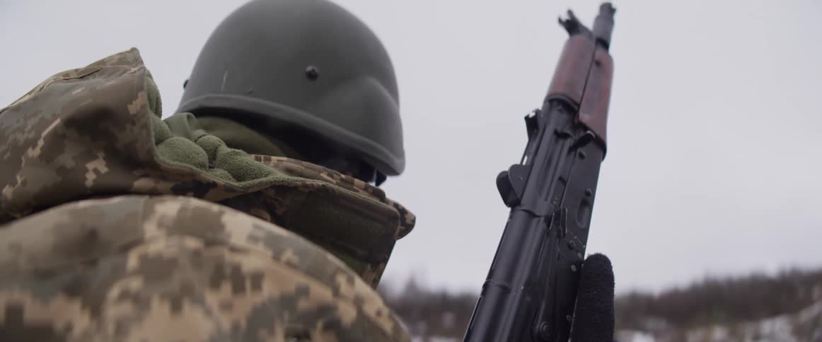 Over the shoulder close-up of a soldier in winter camouflage and helmet holding a rifle
