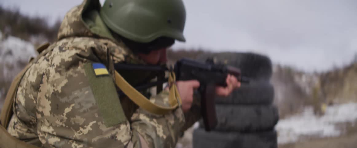 A Ukrainian soldier in a helmet and winter camouflage fires a rifle during military exercises in slow motion