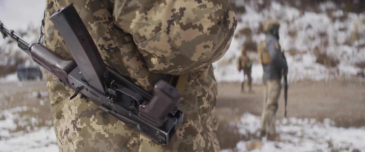 A slow motion close-up shows a soldier in pixelated camouflage holding a rifle while other soldiers train in a snowy landscape
