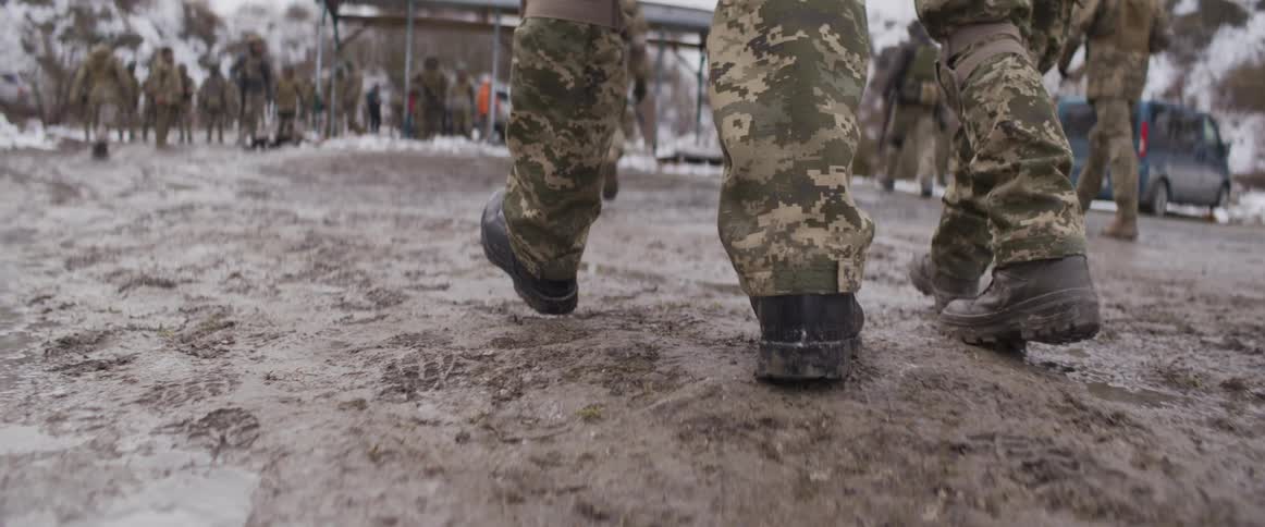 A soldier's combat boot lands in a muddy puddle in super slow motion during a military exercise