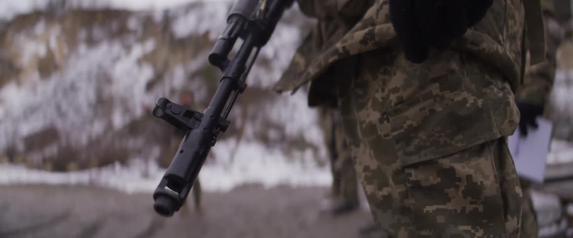 A soldier in camouflage holds a rifle downwards while standing guard in a snowy landscape