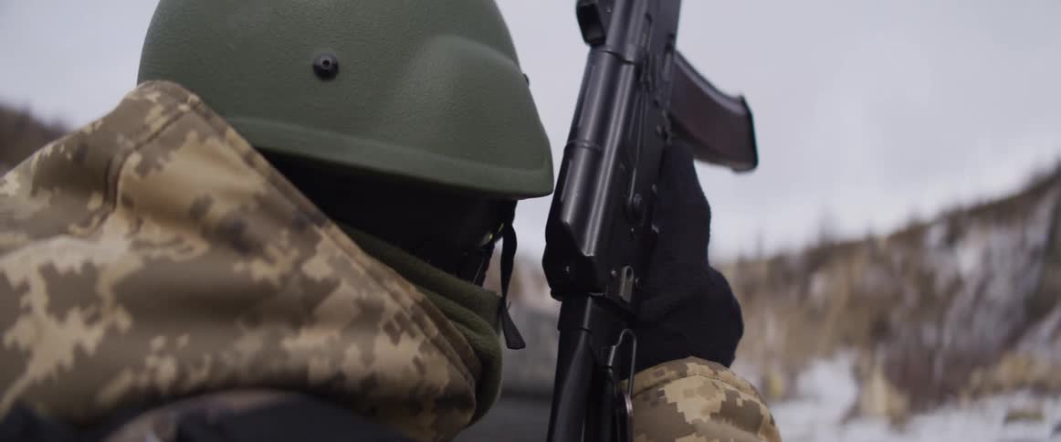 Slow motion over-the-shoulder view of a soldier in winter camouflage holding an assault rifle
