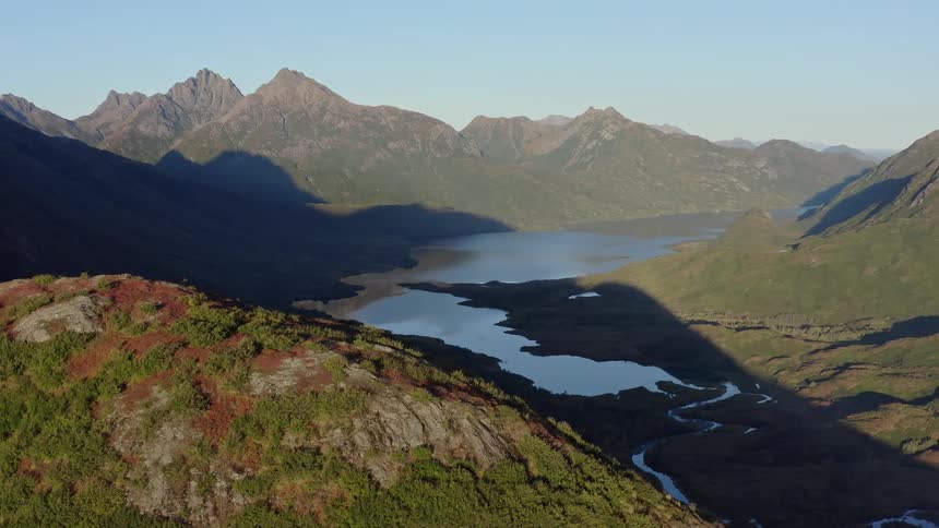 An expansive aerial view of a pristine lake and a winding river nestled in a vast, sunlit mountain valley