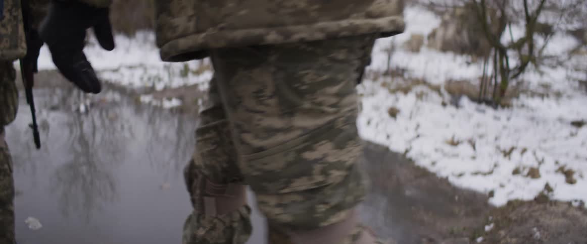 Slow motion shot of two armed soldiers in camouflage patrolling along a snowy riverbank in winter