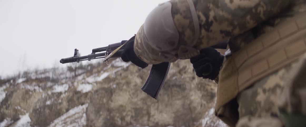 Slow motion close-up of a soldier in camouflage firing an assault rifle in a winter setting