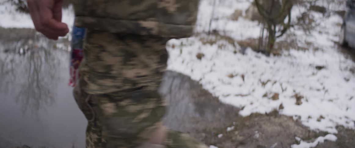 A soldier in full military gear with a weapon walks through a snowy landscape in slow motion