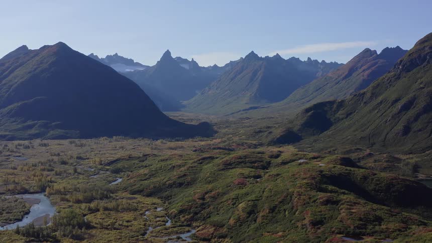 A slow aerial pullback reveals a stunning, vast mountain valley in autumn with a meandering river under a clear blue sky