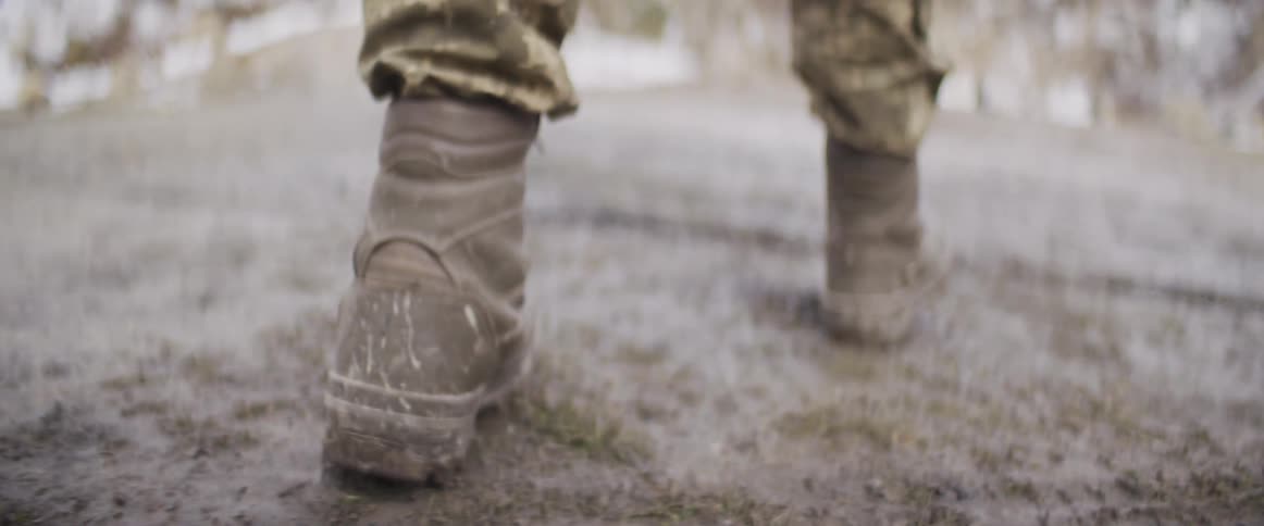 Close-up slow motion shot of a soldier's muddy combat boots walking through wet and snowy terrain